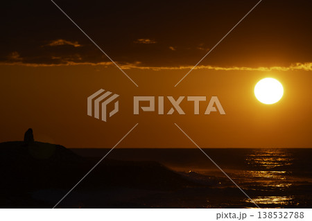 Silhouette of person sitting by sea at intense red sunset with bright sun and reflection on water, dramatic sky and waves, emotional seascape with copy space, solitude and contemplation concept Silhouette of person sitting by sea at intense red sunset with bright sun and reflection on water, dramatic sky and waves, emotional seascape with copy space, solitude and contemplation concept 138532788