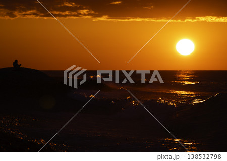 Silhouette of person sitting by sea at intense red sunset with bright sun and reflection on water, dramatic sky and waves, emotional seascape with copy space, solitude and contemplation concept Silhouette of person sitting by sea at intense red sunset with bright sun and reflection on water, dramatic sky and waves, emotional seascape with copy space, solitude and contemplation concept 138532798