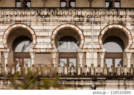 Historic stone building facade with arched windows and decorative columns, classic architecture details with symmetry and texture, old city exterior design with ornamental balcony and arches Historic stone building facade with arched windows and decorative columns, classic architecture details with symmetry and texture, old city exterior design with ornamental balcony and arches 138532800