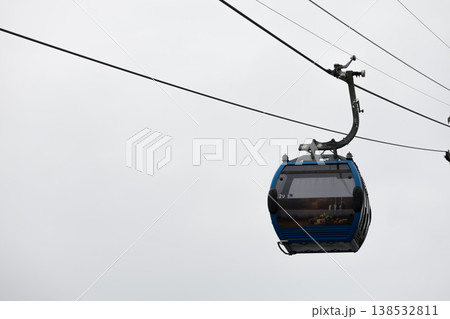 Blue cable car cabin suspended on ropeway against cloudy sky, modern gondola lift transport, minimal composition with copy space, aerial transportation concept in urban or mountain environment Blue cable car cabin suspended on ropeway against cloudy sky, modern gondola lift transport, minimal composition with copy space, aerial transportation concept in urban or mountain environment 138532811