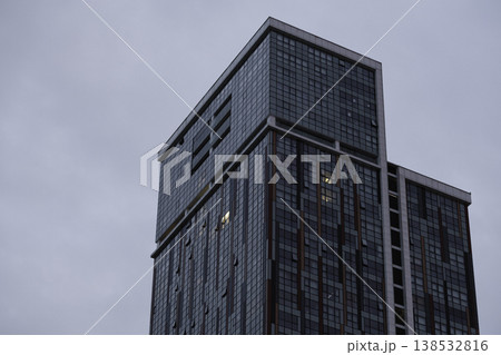 Modern glass skyscraper with geometric facade and reflective windows against overcast sky, contemporary urban architecture with clean lines, minimal cityscape composition, corporate building exterior 138532816