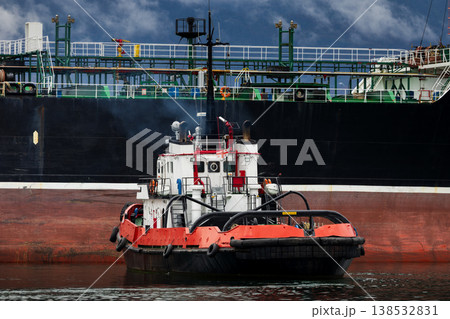 Tugboat assisting large cargo vessel in harbor, maritime transport and port operations, industrial shipping logistics scene with powerful tug pushing ship hull on calm water Tugboat assisting large cargo vessel in harbor, maritime transport and port operations, industrial shipping logistics scene with powerful tug pushing ship hull on calm water 138532831