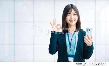 スマートフォンを持ってOKポーズをする笑顔の女性・ビジネスウーマン スマートフォンを持ってOKポーズをする笑顔の女性・ビジネスウーマン 138534647