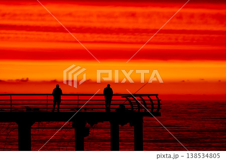 Silhouette of fisherman on pier at sunset over sea, dramatic red sky and ocean horizon, peaceful fishing scene, solitude and lifestyle concept with calm evening atmosphere Silhouette of fisherman on pier at sunset over sea, dramatic red sky and ocean horizon, peaceful fishing scene, solitude and lifestyle concept with calm evening atmosphere 138534805