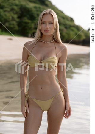 Blonde woman in bikini on beach. Fashionable model posing at ocean coast Blonde woman in bikini on beach. Fashionable model posing at ocean coast 138535063