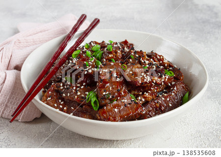 Crispy beef, with green onions and sesame seeds, in a bowl with chopsticks, on a textured surface, on a light background, no people Crispy beef, with green onions and sesame seeds, in a bowl with chopsticks, on a textured surface, on a light background, no people 138535608