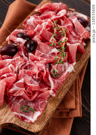 Freshly cut dried meat, served with olives and herbs, on a wooden chopping board, no people, Freshly cut dried meat, served with olives and herbs, on a wooden chopping board, no people, 138535609