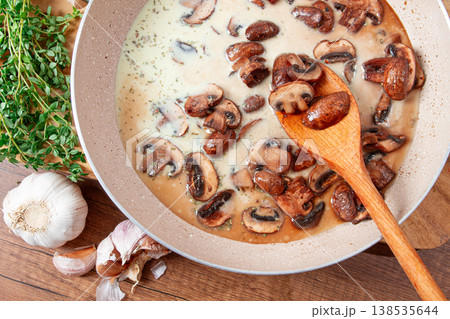 Mushrooms cooking in cream sauce with garlic and herbs on a wooden table 138535644