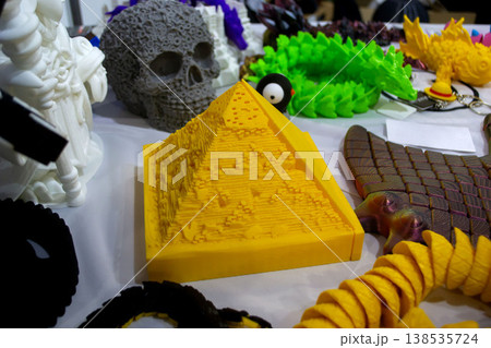 3D printed different art objects. Objects printed on 3D printer from melted colored plastic. Model yellow pyramid created on 3D printer from threads of molten plastic. Modern additive technologies 138535724