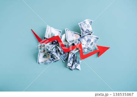Red arrow points downward through pile of crumpled banknotes on blue background. Macroeconomic instability, market collapse, debt crisis. Red arrow points downward through pile of crumpled banknotes on blue background. Macroeconomic instability, market collapse, debt crisis. 138535867