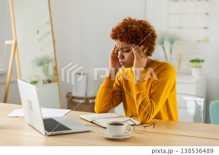 African woman touching temples experiencing stress. Girl at home office tired of working feeling headache sick rubbing temples forehead. Long laptop usage computer vision syndrome. Office syndrome 138536489