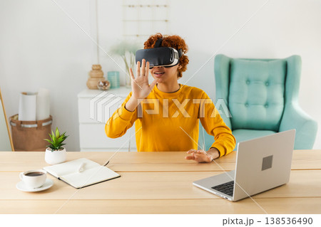 African American young woman wearing using virtual reality metaverse VR glasses headset at home. Girl touching air during VR experience on virtual reality helmet. Simulation hi-tech videogame concept African American young woman wearing using virtual reality metaverse VR glasses headset at home. Girl touching air during VR experience on virtual reality helmet. Simulation hi-tech videogame concept 138536490