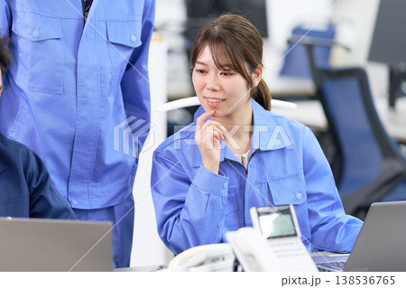 明るい表情でパソコンのデータを見る作業服姿の女性スタッフ 138536765