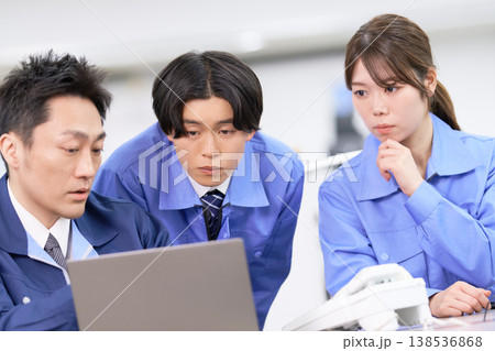 ノートパソコンを囲んで真剣な表情で打ち合わせをする作業着の男女3人 ノートパソコンを囲んで真剣な表情で打ち合わせをする作業着の男女3人 138536868