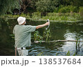 Man with fishing rod near the lake fishing at summer. Fisherman catch a fish. Man wearing khaki clothes and a cap. 138537684