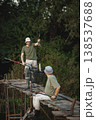 Father and adult son with fishing rods near the lake fishing at summer. Fishermen sitting on a footbridge. Men wearing khaki clothes and a caps. 138537688