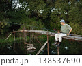 Man with fishing rod near the lake fishing at summer. Fisherman sitting on a footbridge. Man wearing khaki clothes and a cap. 138537690