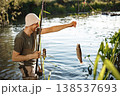 Man with fishing rod near the lake fishing at summer. Fisherman catch a fish. Man wearing khaki clothes and a cap. 138537693