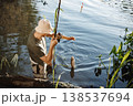 Man with fishing rod near the lake fishing at summer. Fisherman enjoying his hobby. Man wearing khaki clothes and a cap. 138537694