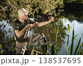 Man with fishing rod near the lake fishing at summer. Fisherman enjoying his hobby. Man wearing khaki clothes and a cap. 138537695
