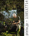 Man with fishing rod near the lake fishing at summer. Fisherman enjoying his hobby. Man wearing khaki clothes and a cap. 138537714