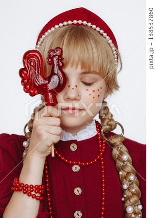 Smiling Caucasian girl with rooster lollipop in Russian folk style outfit on light background 138537860