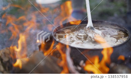 Cast-iron cauldron with soup at the stake in the courtyard. Summer day and dinner in the fresh air near the flower bed. Homemade bricks with cast iron lid. Cast iron with soup at the stake. 138537958