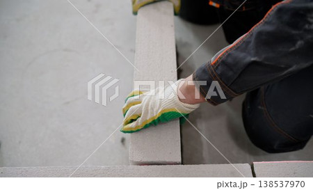 A construction worker's gloved hand laying an autoclaved aerated concrete block to build an interior wall. 138537970