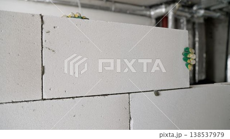 Builder laying a large white aerated concrete block on an interior partition wall. Builder laying a large white aerated concrete block on an interior partition wall. 138537979