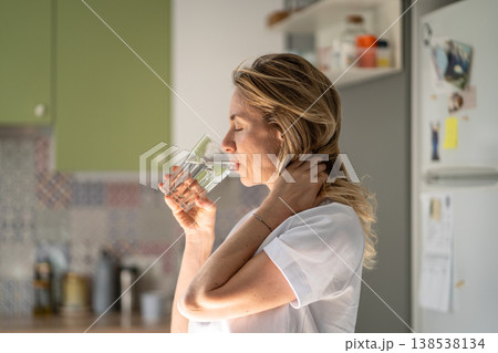 Relaxed positive woman sipping fresh water from glass, slow morning routine after healthy sleep. 138538134