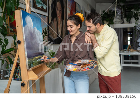 Creative couple enjoying painting, curious husband watching wife drawing oil landscape on canvas. 138538156