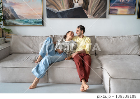 Cheerful husband and wife married couple sit on cozy couch in living room enjoying romantic moment. 138538189