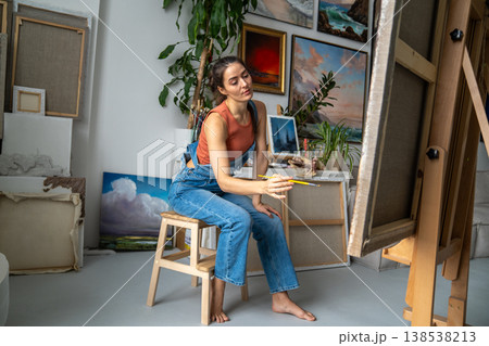 Skillful female artist painting picture on easel with paintbrush, fully engaged in creative process. Skillful female artist painting picture on easel with paintbrush, fully engaged in creative process. 138538213