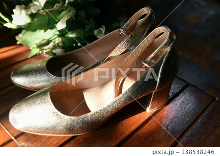 Golden bridal shoes on wooden table with greenery sunlight shine 138538246