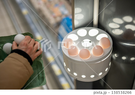 Unrecognizable female customer in shop checking raw eggs contents in ovoscope candling station. Unrecognizable female customer in shop checking raw eggs contents in ovoscope candling station. 138538266