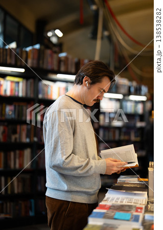Focused smart man reviewing textbook in trendy bookshop, inspecting through content of popular novel 138538282