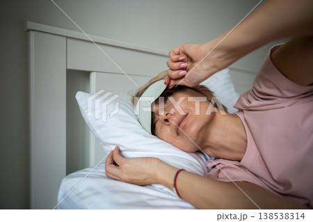 Sleepy relaxed woman waking up in early morning and peeking out from eye mask lying in bed. 138538314