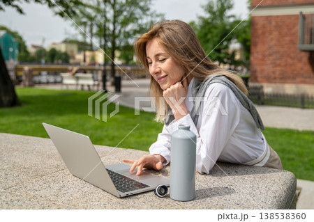Smiling happy businesswoman enjoys working on laptop outdoors on summer day, benefits of remote work 138538360