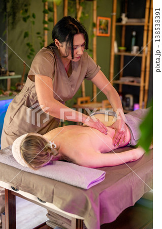 Attentive female masseuse therapist carefully massaging back muscles for woman lying on spa bed. 138538391