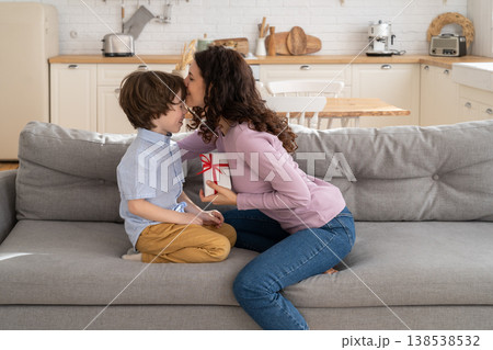 Mom kissing child, receives wrapped gift box with red bow from son for her birthday. Loving family. 138538532