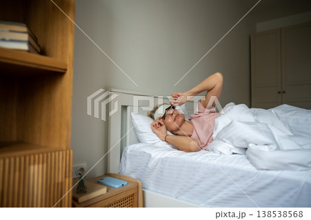 Sleepy relaxed woman waking up in early morning and peeking out from eye mask lying in bed. Sleepy relaxed woman waking up in early morning and peeking out from eye mask lying in bed. 138538568