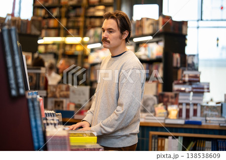 Booklover man customer buying books in bookshop, looking at various publications on display in store. Booklover man customer buying books in bookshop, looking at various publications on display in store. 138538609