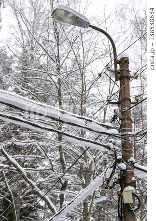 Several utility power lines and cables hanging covered in snow against winter forest background. Several utility power lines and cables hanging covered in snow against winter forest background. 138538634
