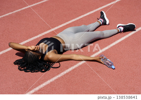 Powerless African American woman in sportswear lies on red track covering eyes with hand from sun Powerless African American woman in sportswear lies on red track covering eyes with hand from sun 138538641