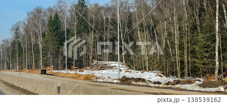Extensive deforestation clearing a natural forest area for the construction of a new highway, showing felled logs, piles of sand, and remaining trees under sparse winter conditions. Extensive deforestation clearing a natural forest area for the construction of a new highway, showing felled logs, piles of sand, and remaining trees under sparse winter conditions. 138539162