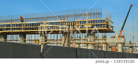 Large concrete road bridge construction site with formwork, rebar, workers, and a mobile crane working on new infrastructure development under a clear blue sky. Large concrete road bridge construction site with formwork, rebar, workers, and a mobile crane working on new infrastructure development under a clear blue sky. 138539180