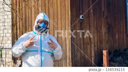 Person wearing protective hazmat suit and respirator mask making peace signs, representing safety, health, and a positive outlook during potential crisis or pandemic situations. 138539215