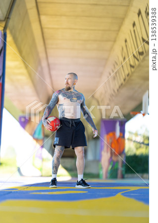 Tattooed man holding old basketball under urban bridge 138539388