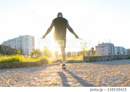 Tattooed man skipping rope during outdoor workout at sunset Tattooed man skipping rope during outdoor workout at sunset 138539425