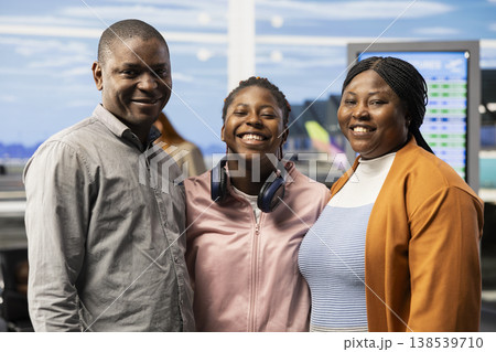 Portrait of black happy family of three passengers in airport waiting area, parents and teenager in good mood preparing for holiday travel. Travelers with suitcases at departure gate. Portrait of black happy family of three passengers in airport waiting area, parents and teenager in good mood preparing for holiday travel. Travelers with suitcases at departure gate. 138539710